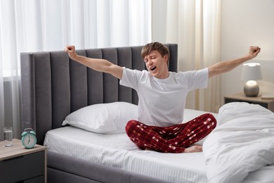 Photo of Young man stretching on bed indoors. Good morning