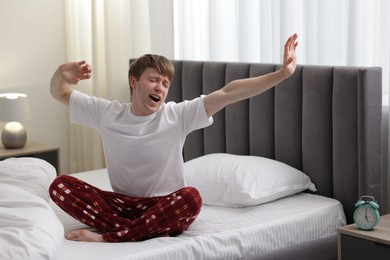 Photo of Young man stretching on bed indoors. Good morning