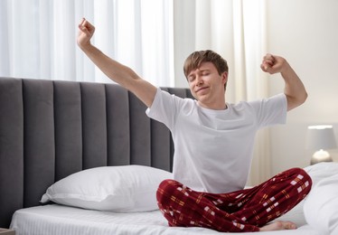 Photo of Young man stretching on bed indoors. Good morning