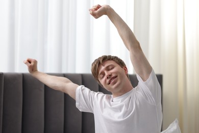 Photo of Happy man stretching on bed indoors. Good morning