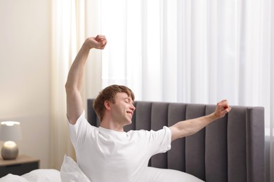 Photo of Happy man stretching on bed indoors. Good morning