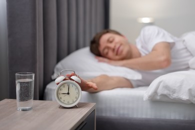 Photo of Man turning off alarm clock in bed indoors, selective focus