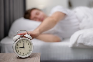 Photo of Man turning off alarm clock in bed indoors, selective focus