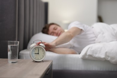 Photo of Man turning off alarm clock in bed indoors, selective focus