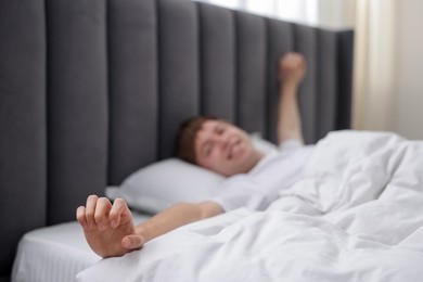Photo of Happy man stretching in bed indoors, selective focus