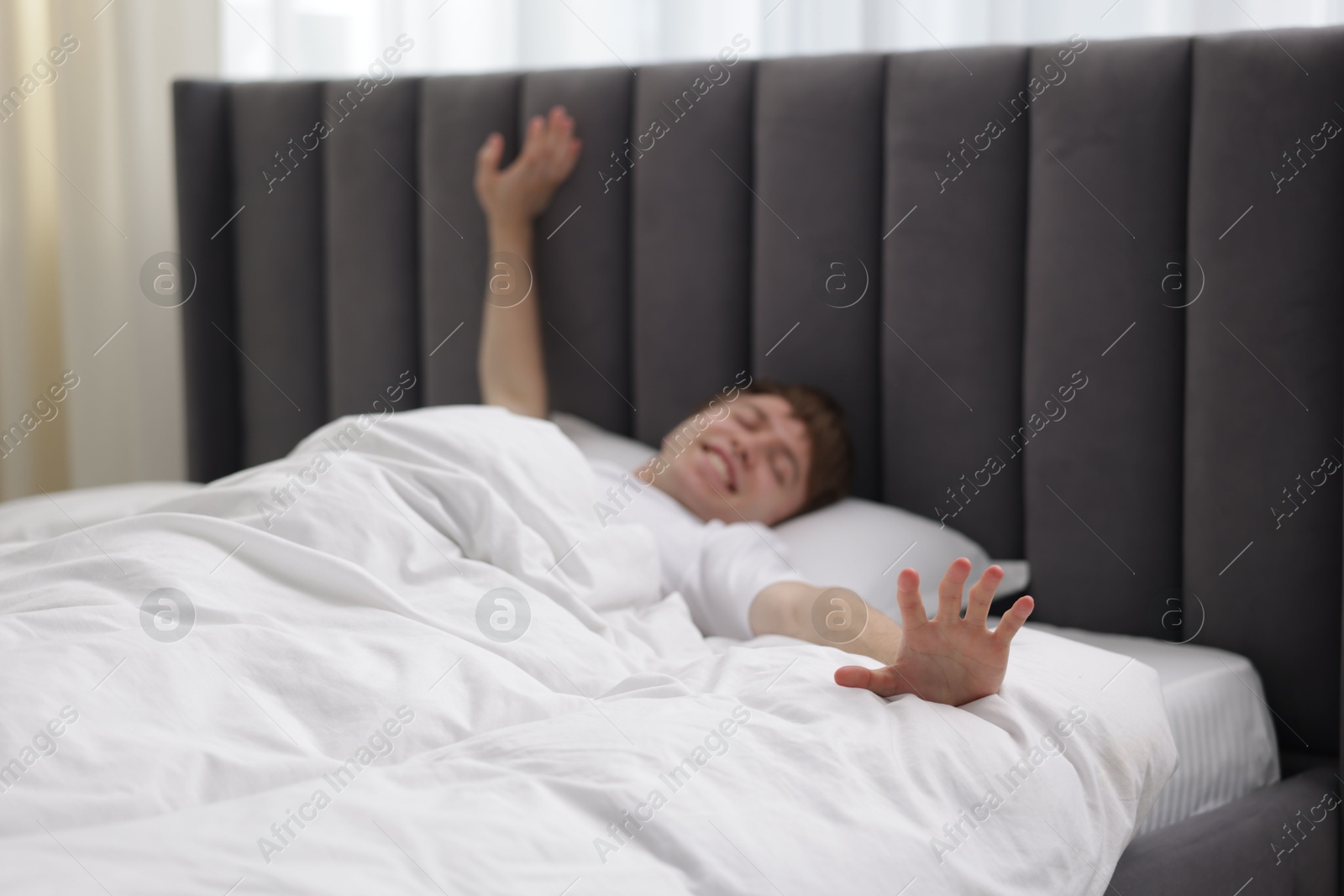 Happy man stretching in bed indoors, selective focus Photo of Happy man stretching in bed indoors, selective focus