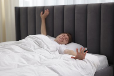 Photo of Happy man stretching in bed indoors, selective focus