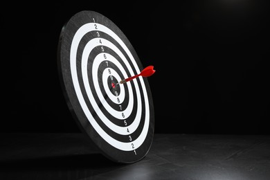 Photo of Targeting. Dart board with arrow on gray surface against black background, space for text