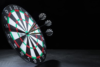 Photo of Targeting. Dart board with arrows on gray surface against black background, space for text