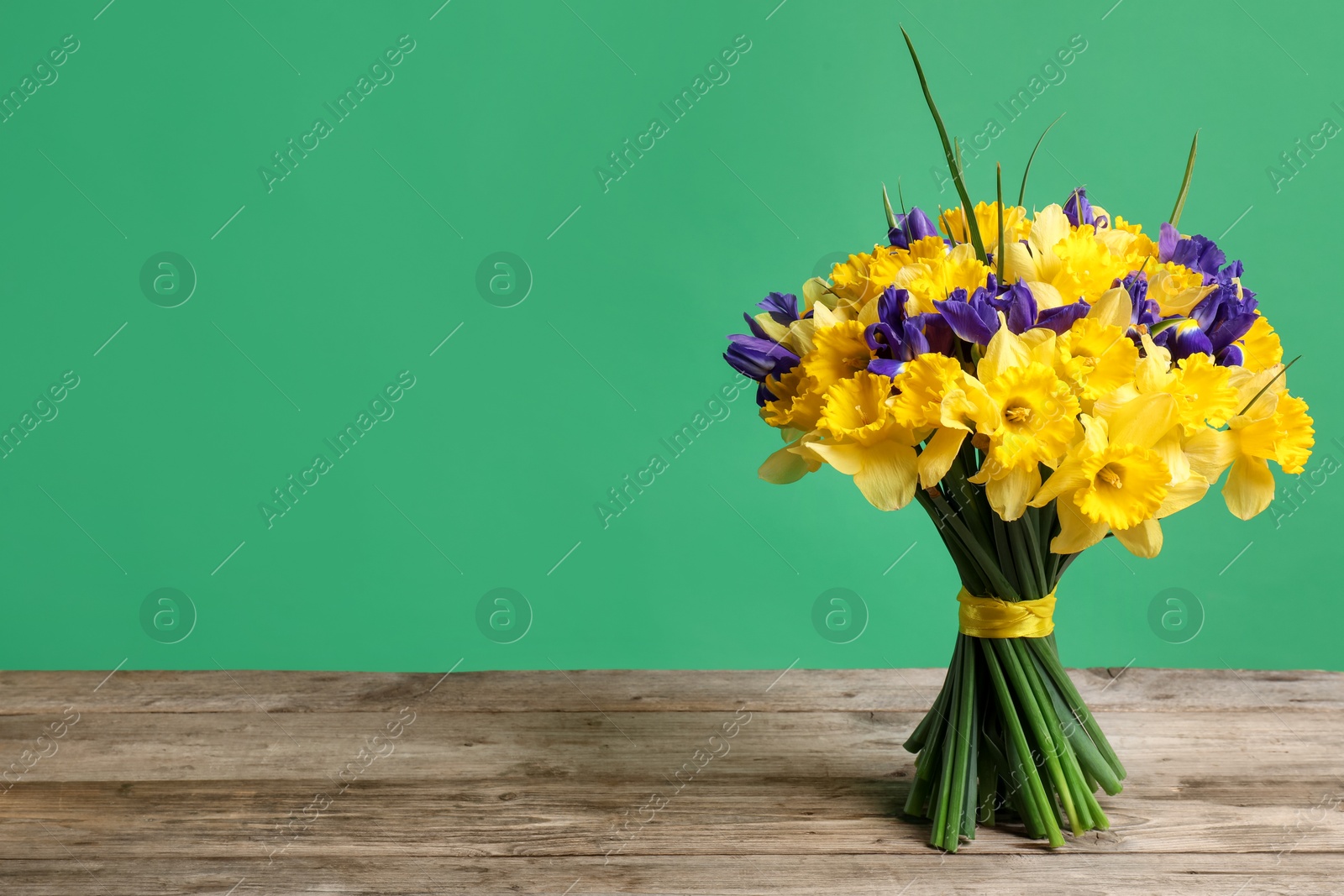 Bunch of beautiful flowers on wooden table against green background. Space for text Photo of Bunch of beautiful flowers on wooden table against green background. Space for text