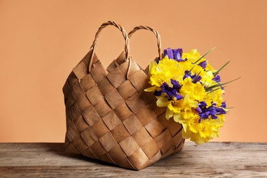 Photo of Wicker basket with beautiful flowers on wooden table against coral background, closeup