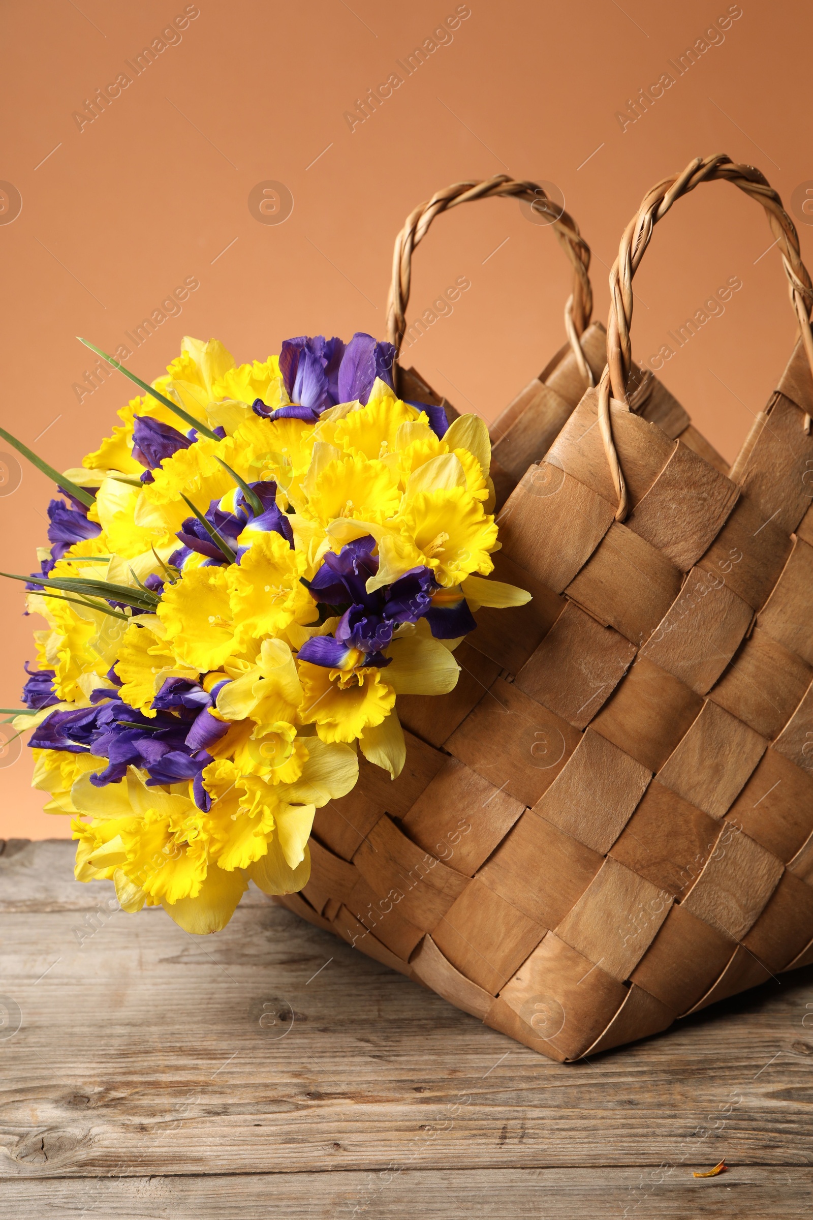 Wicker basket with beautiful flowers on wooden table against coral background, closeup Photo of Wicker basket with beautiful flowers on wooden table against coral background, closeup