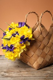Photo of Wicker basket with beautiful flowers on wooden table against coral background, closeup