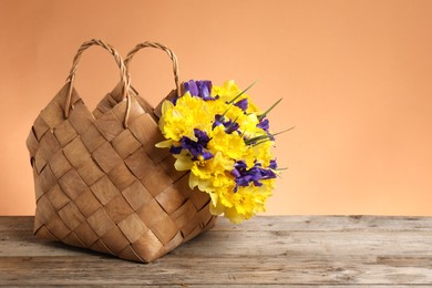Photo of Wicker basket with beautiful flowers on wooden table against coral background. Space for text