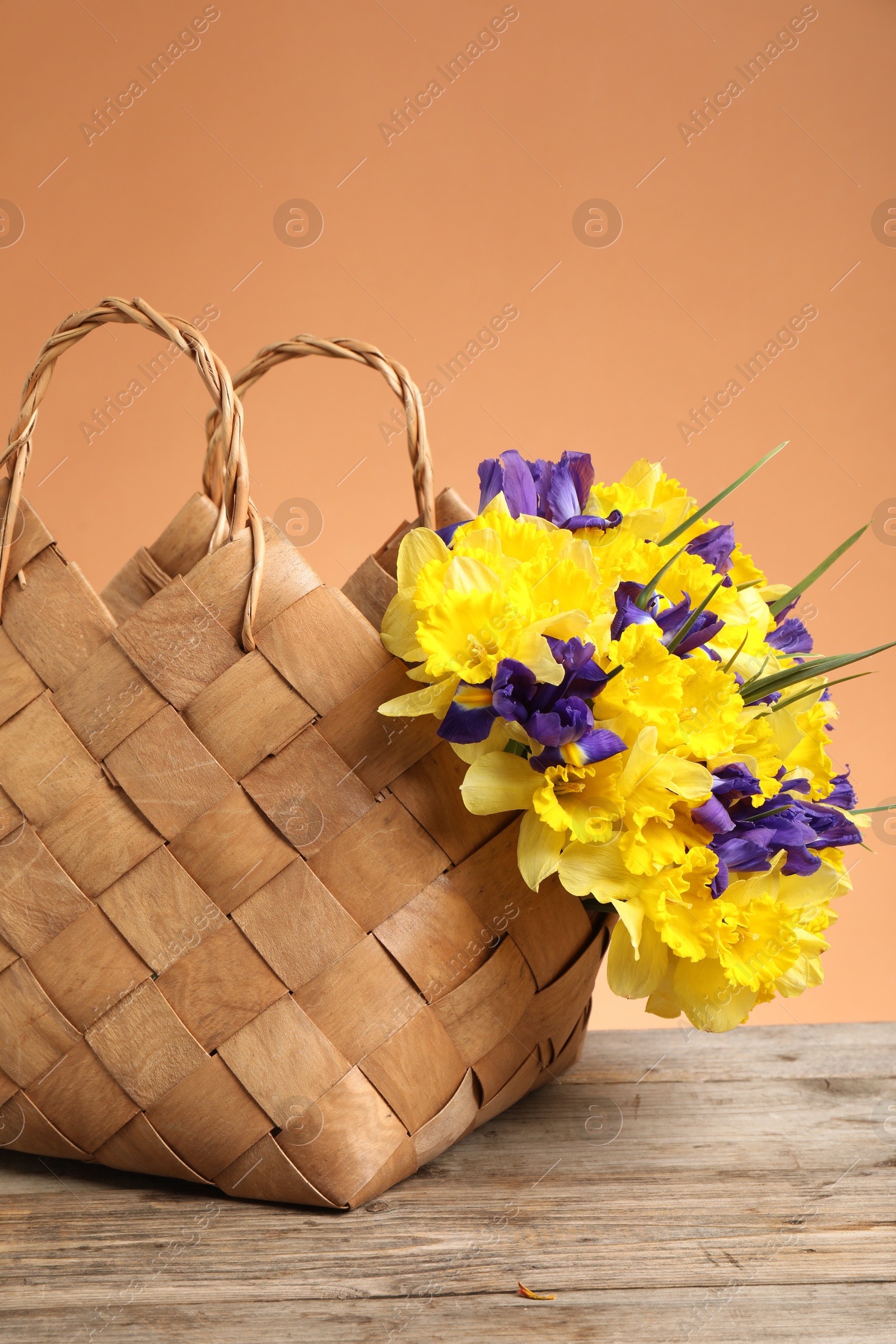 Wicker basket with beautiful flowers on wooden table against coral background, closeup Photo of Wicker basket with beautiful flowers on wooden table against coral background, closeup