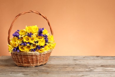 Photo of Wicker basket with beautiful flowers on wooden table against coral background. Space for text