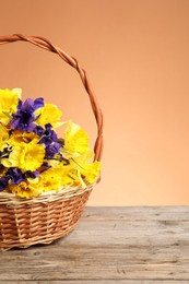 Photo of Wicker basket with beautiful flowers on wooden table against coral background. Space for text