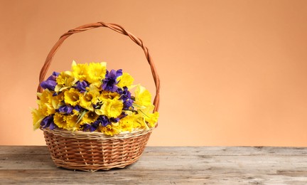 Photo of Wicker basket with beautiful flowers on wooden table against coral background. Space for text