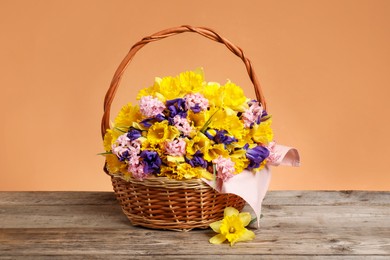 Photo of Wicker basket with beautiful flowers on wooden table against coral background