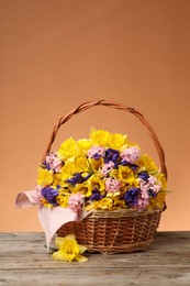 Photo of Wicker basket with beautiful flowers on wooden table against coral background