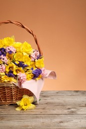 Photo of Wicker basket with beautiful flowers on wooden table against coral background, closeup. Space for text