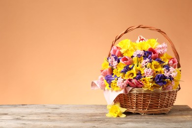 Photo of Wicker basket with beautiful flowers on wooden table against coral background. Space for text
