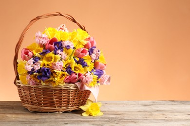 Photo of Wicker basket with beautiful flowers on wooden table against coral background. Space for text