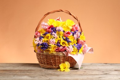 Photo of Wicker basket with beautiful flowers on wooden table against coral background