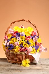 Photo of Wicker basket with beautiful flowers on wooden table against coral background