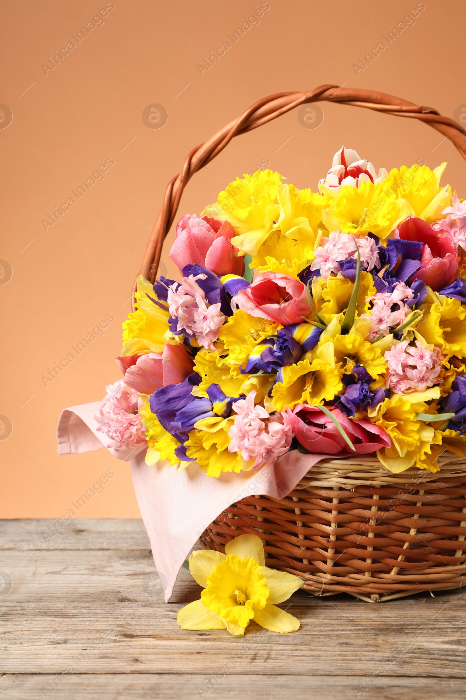 Wicker basket with beautiful flowers on wooden table against coral background, closeup Photo of Wicker basket with beautiful flowers on wooden table against coral background, closeup