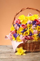 Photo of Wicker basket with beautiful flowers on wooden table against coral background, closeup
