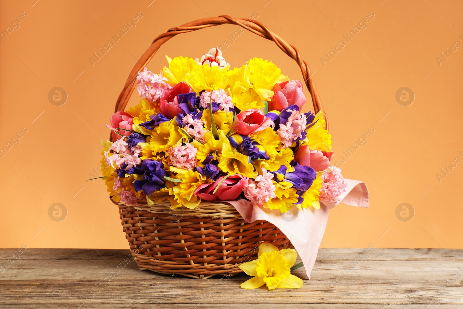 Wicker basket with beautiful flowers on wooden table against coral background, closeup Photo of Wicker basket with beautiful flowers on wooden table against coral background, closeup