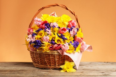 Photo of Wicker basket with beautiful flowers on wooden table against coral background, closeup