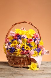 Photo of Wicker basket with beautiful flowers on wooden table against coral background