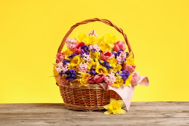 Photo of Wicker basket with beautiful flowers on wooden table against yellow background