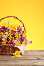 Photo of Wicker basket with beautiful flowers on wooden table against yellow background