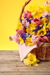 Photo of Wicker basket with beautiful flowers on wooden table against yellow background, closeup
