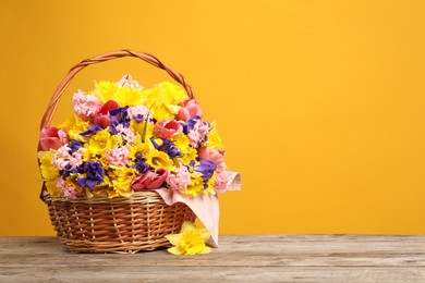 Photo of Wicker basket with beautiful flowers on wooden table against yellow background. Space for text