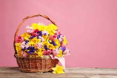 Photo of Wicker basket with beautiful flowers on wooden table against pink background. Space for text