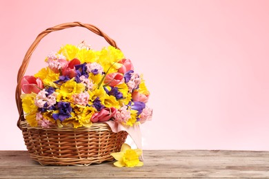 Photo of Wicker basket with beautiful flowers on wooden table against pink background. Space for text