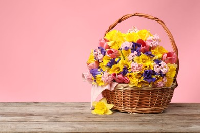 Photo of Wicker basket with beautiful flowers on wooden table against pink background. Space for text