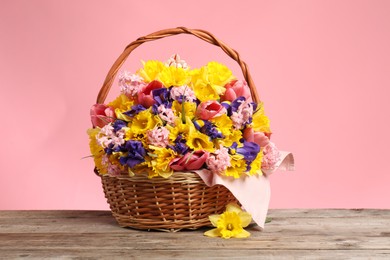 Photo of Wicker basket with beautiful flowers on wooden table against pink background