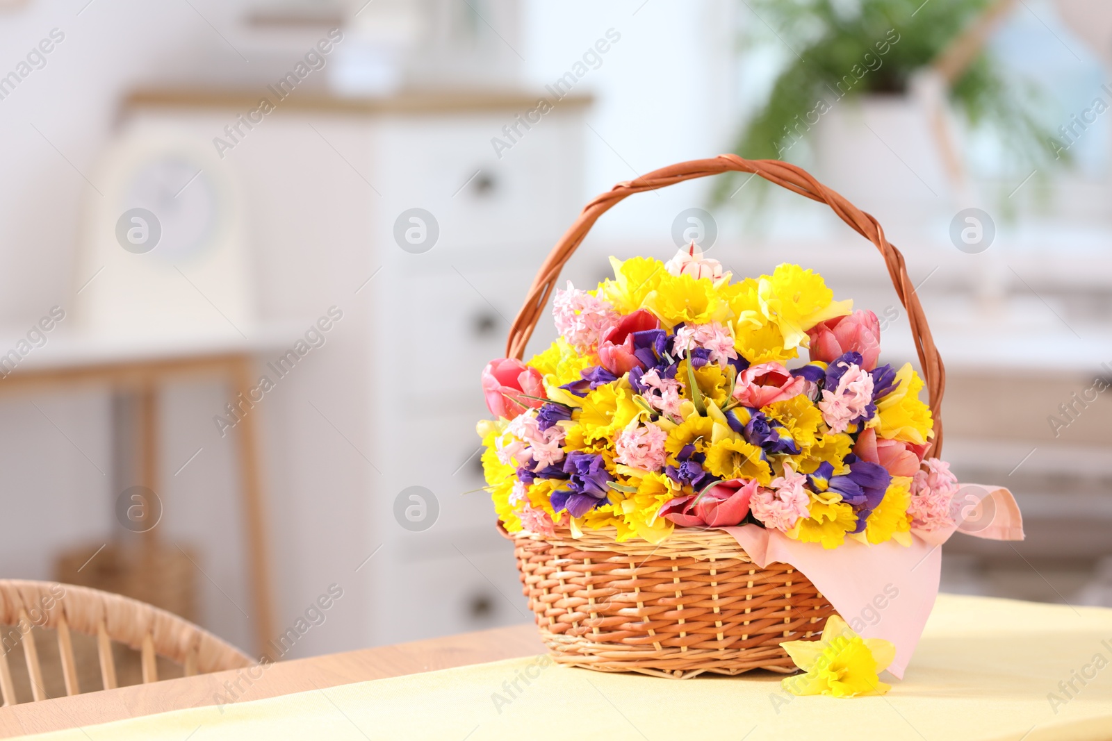 Wicker basket with beautiful flowers on table indoors. Space for text Photo of Wicker basket with beautiful flowers on table indoors. Space for text