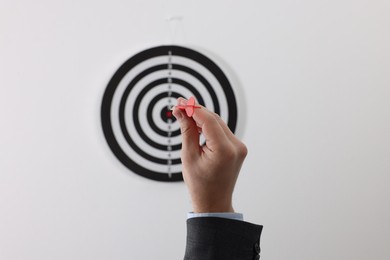 Photo of Targeting. Man with arrow aiming at dart board on light background, closeup