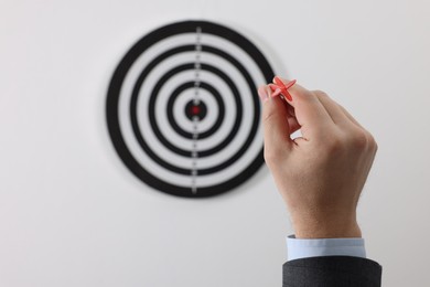 Photo of Targeting. Man with arrow aiming at dart board on light background, closeup