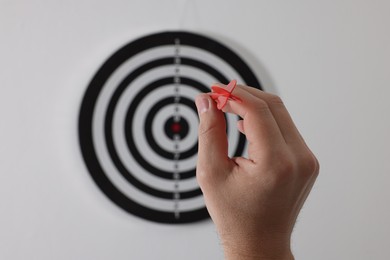 Photo of Targeting. Man with arrow aiming at dart board on light background, closeup