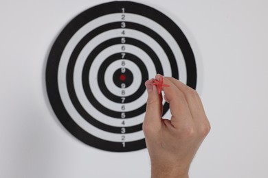 Photo of Targeting. Man with arrow aiming at dart board on light background, closeup