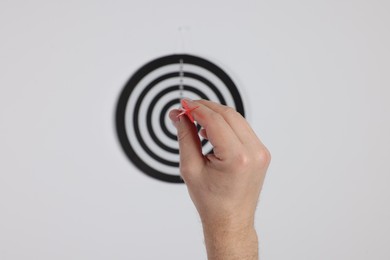 Photo of Targeting. Man with arrow aiming at dart board on light background, closeup