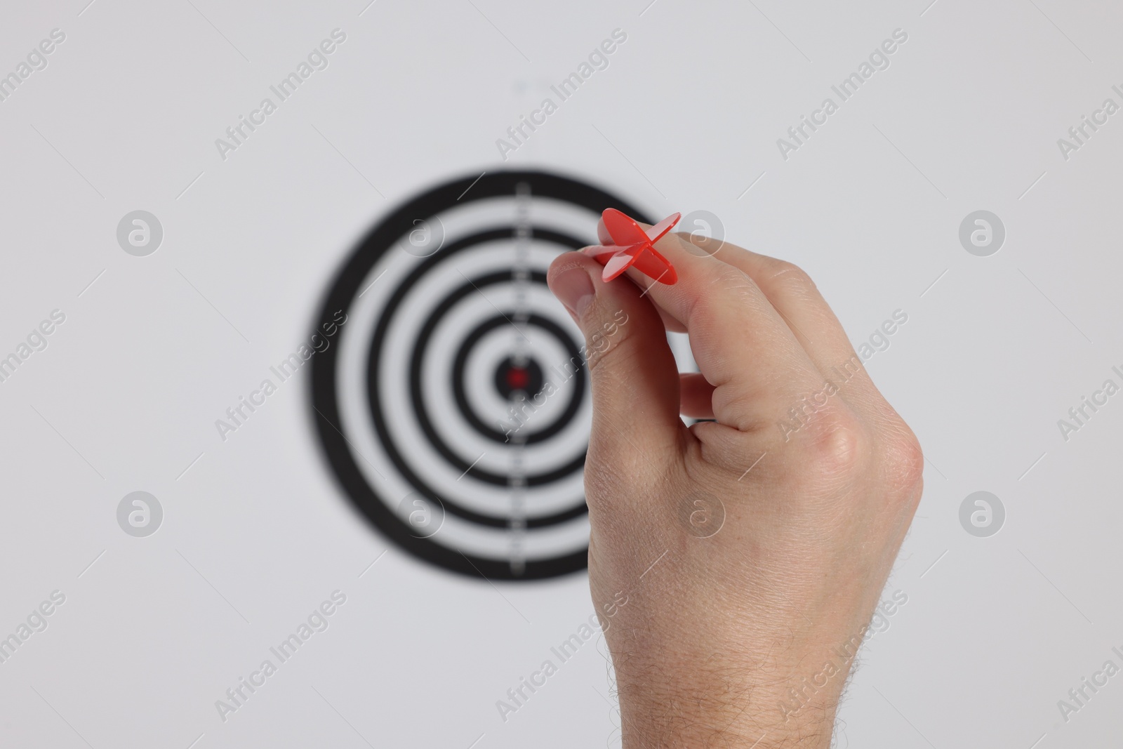 Photo of Targeting. Man with arrow aiming at dart board on light background, closeup