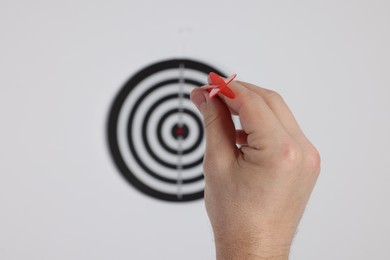 Photo of Targeting. Man with arrow aiming at dart board on light background, closeup